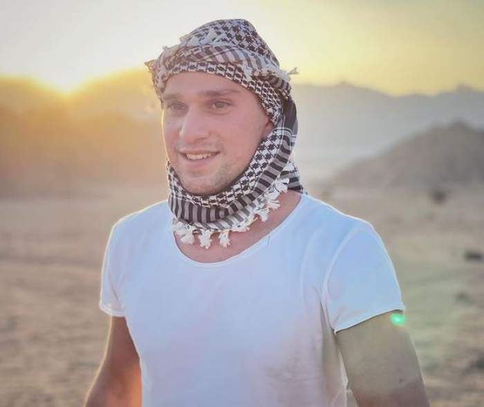Vlad Gherman se află în Egipt. Artistul e îmbrăcat cu un tricou alb și poartă pe cap o eșarfă cu alb și negru.