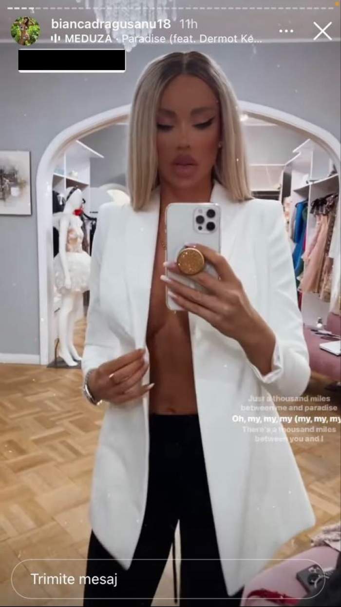 Bianca Drăgușanu poartă niște pantaloni negri și un sacou alb, fără sutien. Vedeta se filmează cu telefonul în oglindă și este într-un atelier de haine.