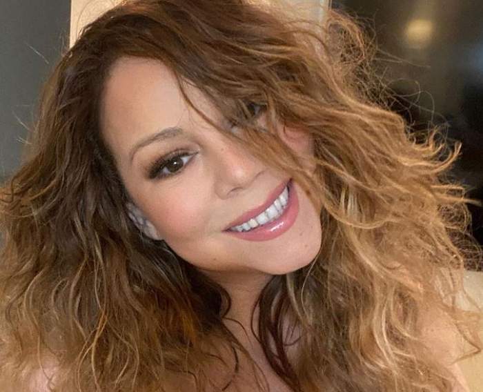 Mariah Carey are părul ondulat. Vedeta își face un selfie și zâmbește larg.
