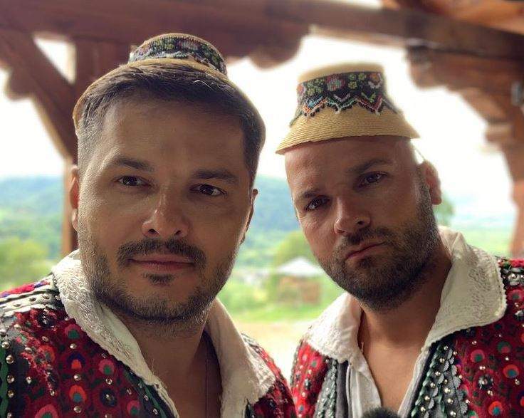 Liviu Vârciu și Andrei Ștefănescu sunt îmbrăcați în port tradițional, cu ie albă, pălării și veste colorate în albastru și roșu. Cei doi își fac un selfie.