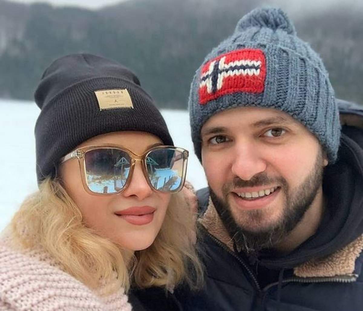 Lora și Ionuț Ghenu își fac un selfie. Cei doi sunt afară. Ea poartă o haină roz și o căciulă neagră, iar el geacă de iarnă și căciulă albastră.
