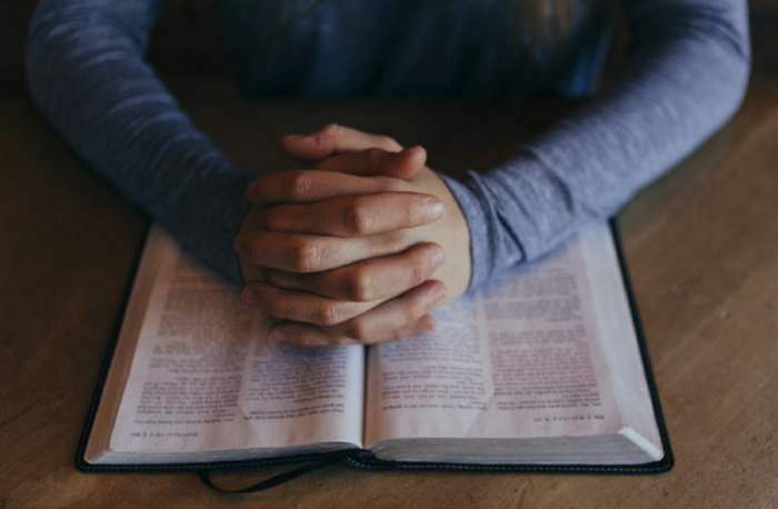 Mâinile încrucișate ale unui bărbat așezate pe o carte de rugăciuni