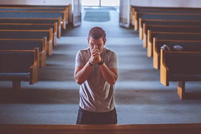 Un bărbat care stă în genunchi și se roagă în biserică