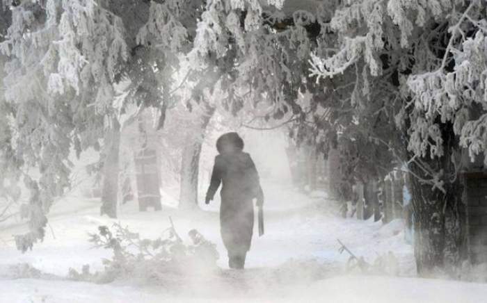 O femeie îmbrăcată în negru, merge prin viscol și zăpadă