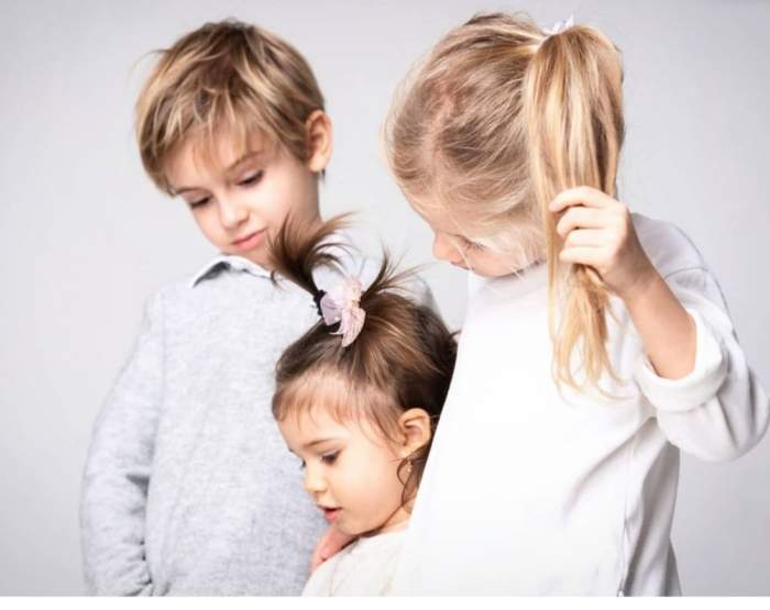 Cei trei copii ai Alinei Pușcaș, îmbrăcați în alb, îmbrățișați și zâmbitori