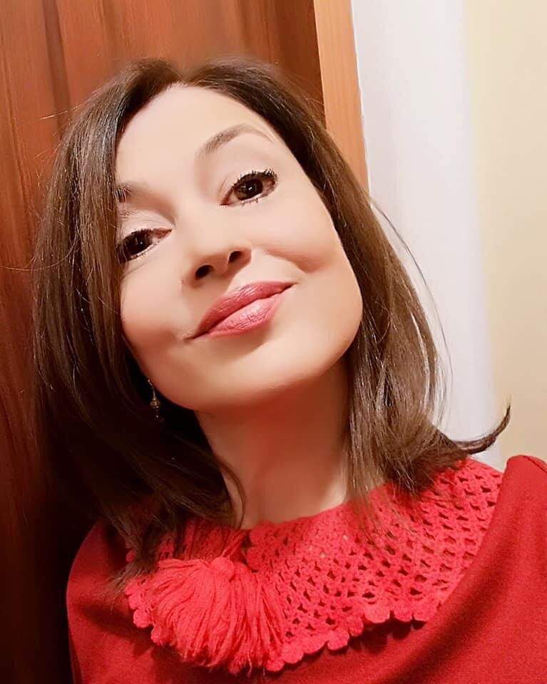 Oana Sîrbu își face un selfie. Vedeta poartă o bluză roșie și zâmbește discret.