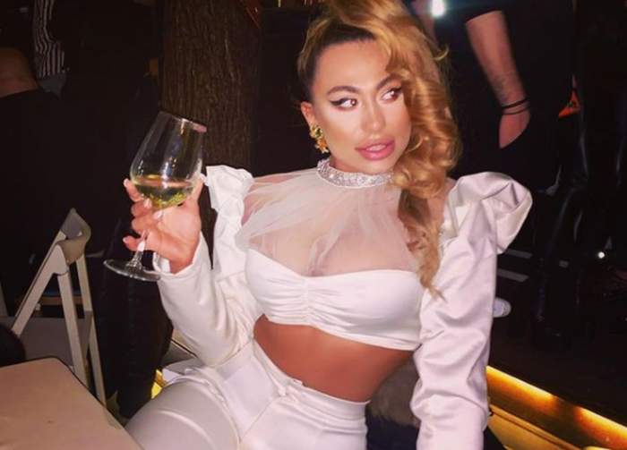 roxana dobritoiu imbracata in alb cu un pahar de alcool in mana la un restaurant