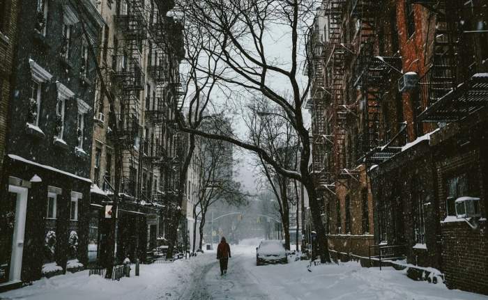 Imagine ilustrativa cu o strada dintr-un oras, acoperita de zapada si un om care sta cu spatele in capatu aleii