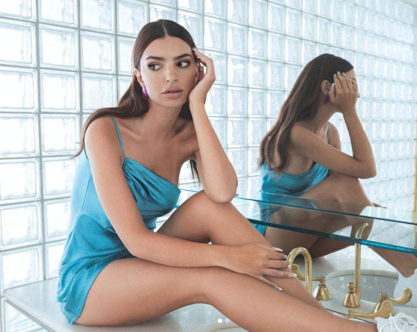 Emily Ratajkowski sta pe o chiuveta din baie, poarta o rochie scurta ablastra cu bretele