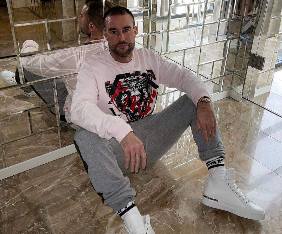 Philipp Plein sta pe jos, poarta pantaloni de trening gri si un hanorac alb