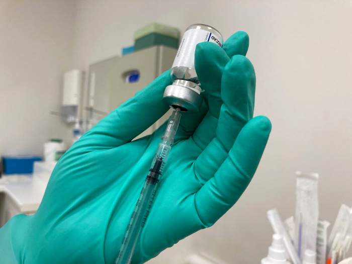 Un medic cu mănușă pe mână ține o sticlă de vaccin