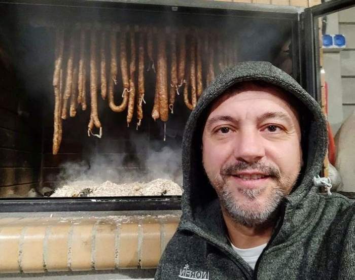 Sorin Bontea își face un selfie. Vedeta poartă un hanorac gri cu gluga pe cap. În spate bucătarului se văd mai mulți cârnați.