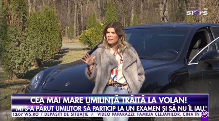 Diana Matei se sprijina de masina ei, este imbracata cu o haina de blana gri, blugi albastri cu o camasa colorata