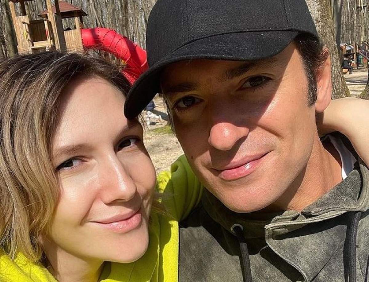 Adela Popescu și Radu Vâlcan sunt în parc. Artista poartă un hanorac galben, iar soțul ei unul gri și o șapcă neagră. Amândoi zâmbesc.