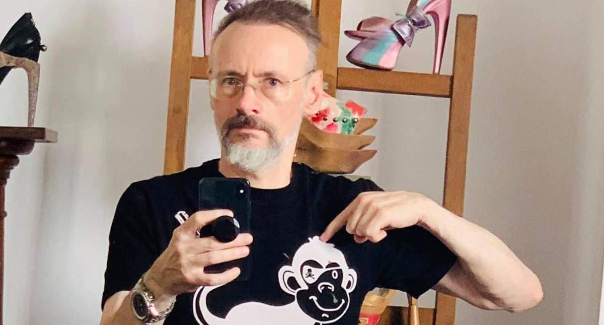 Mihai Albu își face o poză în oglindă cu telefonul. Creatorul de modă poartă un tricou negru pe care e desenată o maimuță albă și arată cu degetul spre ea.