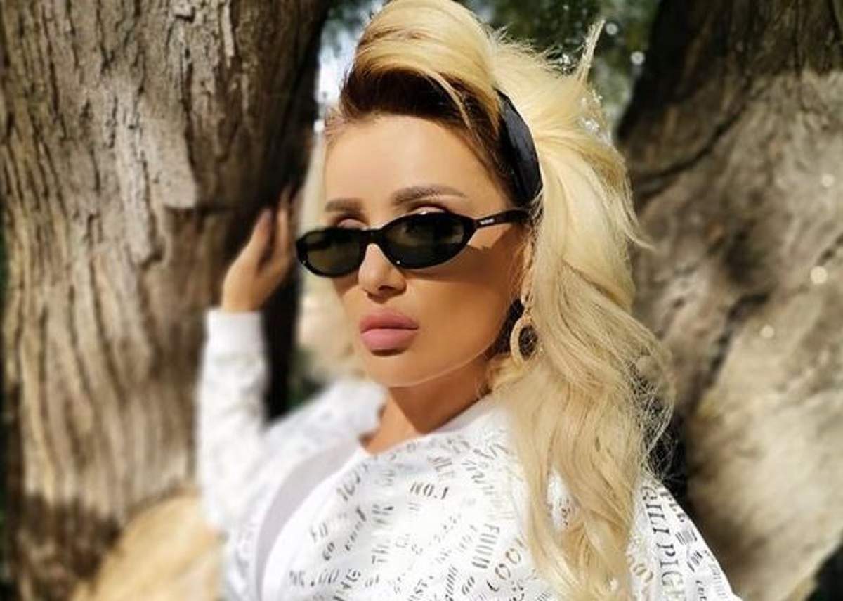 Bianca Rus este în parc. Vedeta poartă o bluză albă și ochelari de soare negri și ține mâna pe un copac.
