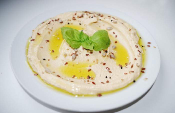 Hummus cu semințe așezat pe o farfurie. Pe deasupra preparatului este pus ulei de măsline.