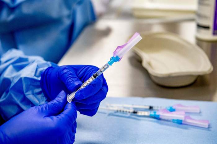 Un cadru medical ține în mână un vaccin anti-covid-19. Acesta poartă mănuși speciale, albastre.