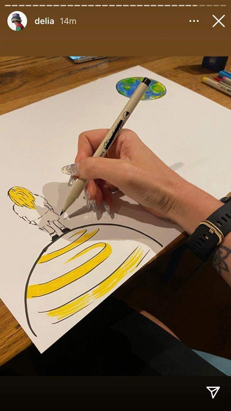 Delia Matache realizează un desen cu o cariocă. Artista colorează o fată așezată pe o planetă.