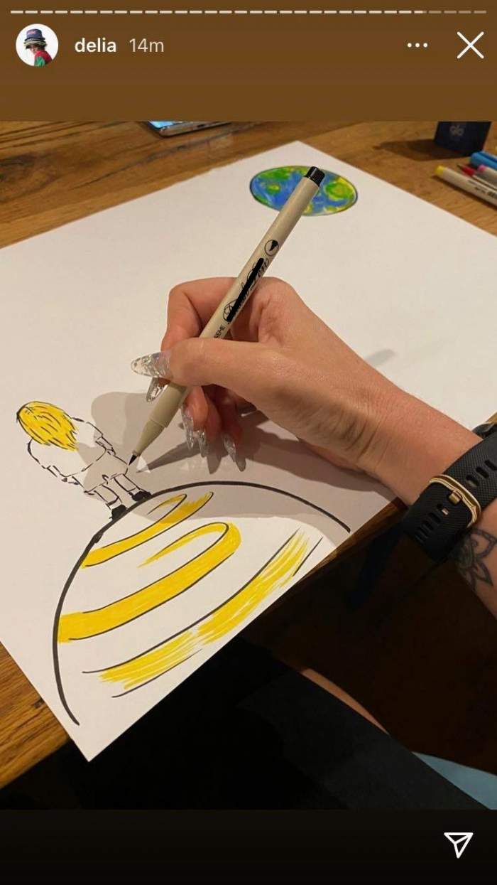 Delia Matache realizează un desen cu o cariocă. Artista colorează o fată așezată pe o planetă.