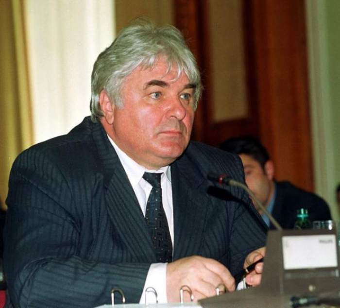 Constantin Simirad poartă un sacou albastru închis, în dungi. Fostul politician are pe dedesubt o cămașă albă și ține în mână un pix.