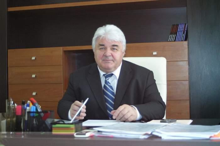 Constantin Simirad stă la birou. Fostul politician poartă cămașă albă, cravată albastră cu dungi albe și cămașă albă.