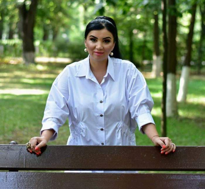 Adriana Bahmuteanu este in parc, este in spatele unei banci si poarta o camasa alba simpla