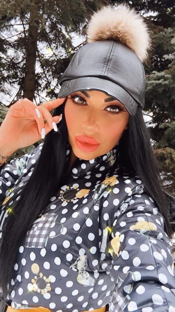 Andreea Podărescu poartă o geacă neagră cu buline albe. Bruneta are pe cap o șapcă neagră cu un puf crem.