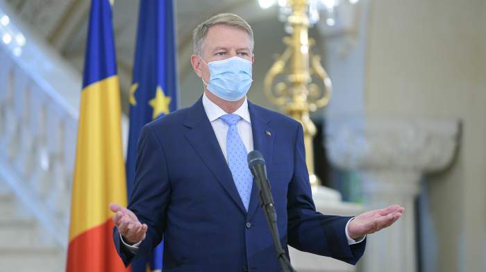Klaus Iohannis, gesticulează în cadrul unei conferințe de presă, cu masca pe față