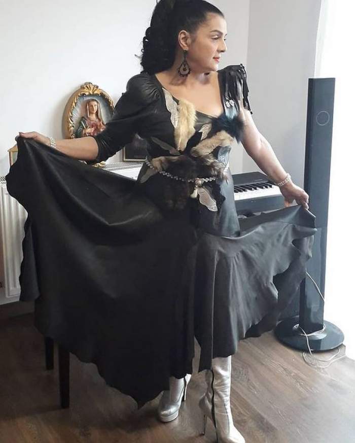 Cornelia Catanga poartă o rochie neagră cu model cu pene la nivelul bustului. Vedeta e încălțată cu cizme argintii și își ține marginile rochiei cu mâinile în aer.