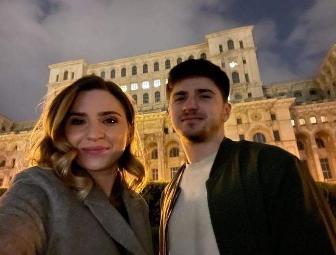 Cristina Ciobănașu și fratele ei, Tudor, se află afară, în fața unei clădiri. Ea poartă un pardesiu gri, iar el un tricou alb și o geacă neagră.