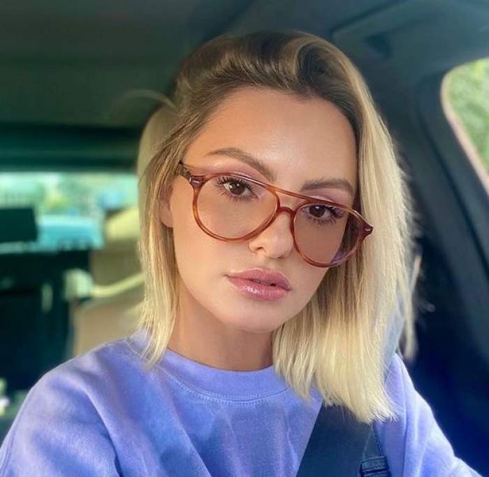 Alexandra Stan e în mașină. Artista poartă ochelari de vedere cu rame roșii și o bluză mov.