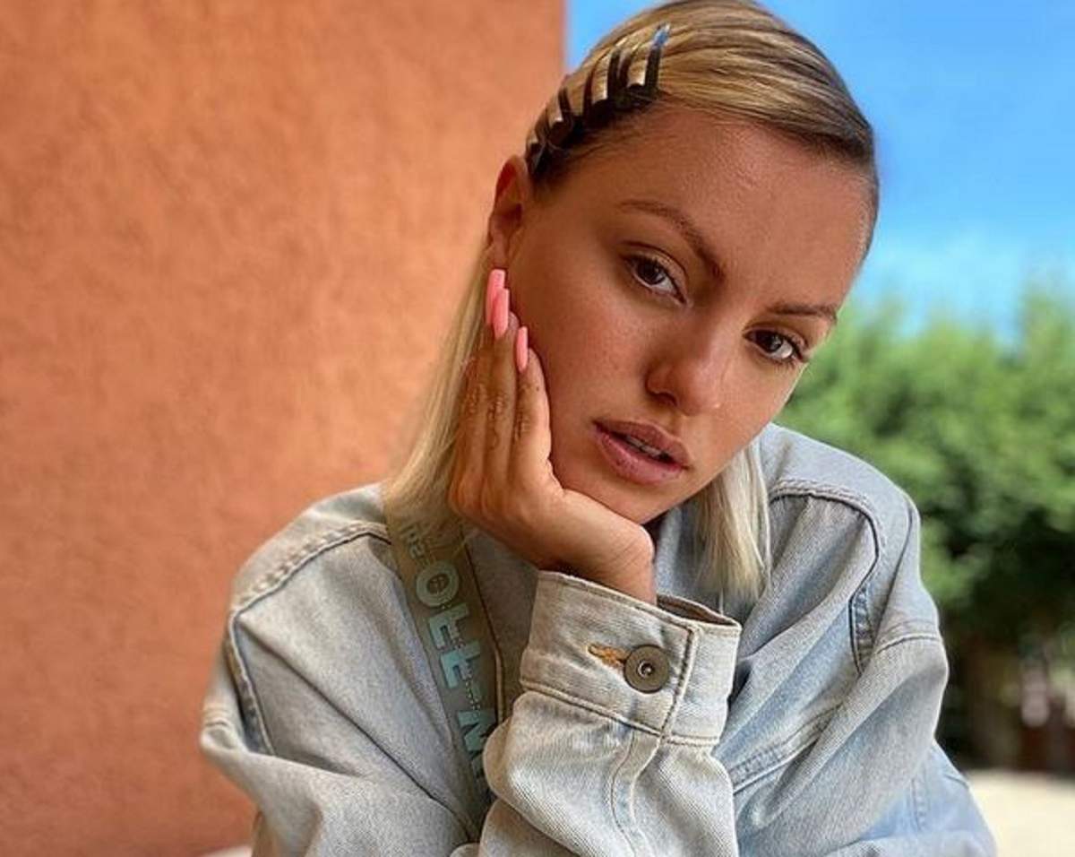 Alexandra Stan poartă o geacă din denim gri. Artista își susține bărbia în palmă.