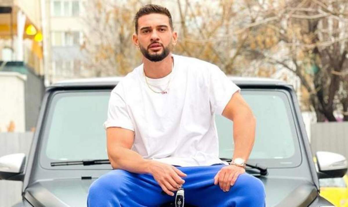 Dorian Popa stă pe mașină, în tricou alb și pantaloni albaștri