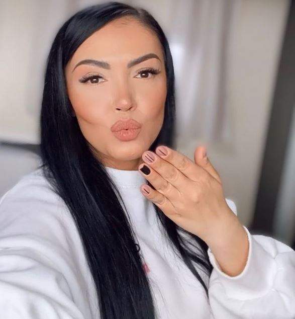 Andreea Mantea își face un selfie. Bruneta ține buzele țuguiate, o mână în aer, de parcă ar trimite „pupici” și poartă o bluză albă.