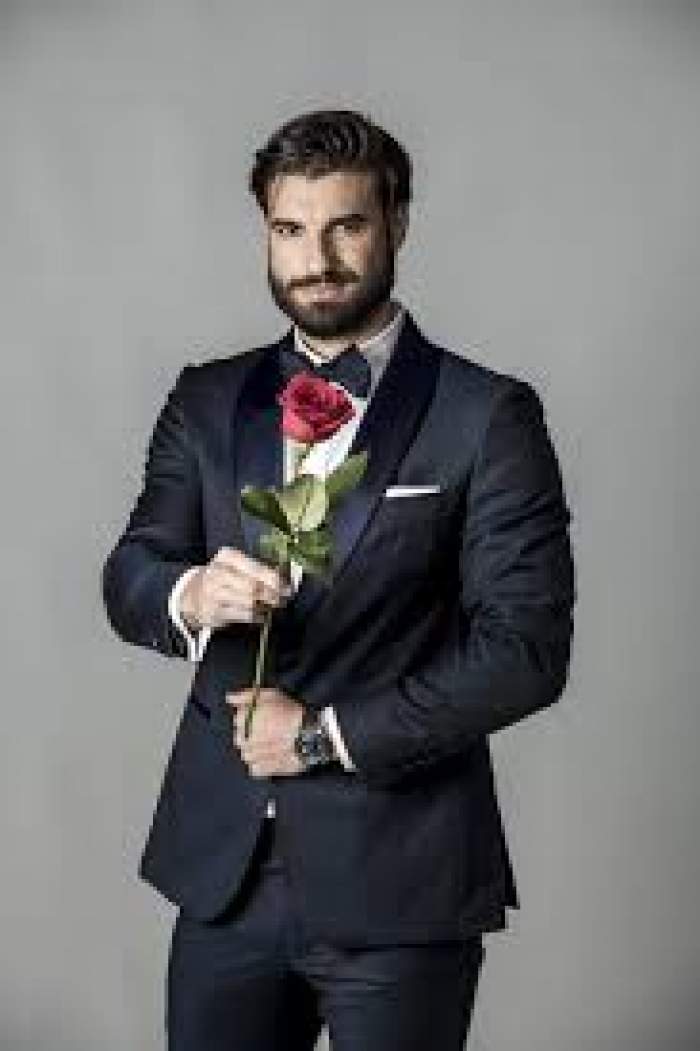 Andi Constantin, în costum negru, cu trandafir roșu în mână, zâmbitor