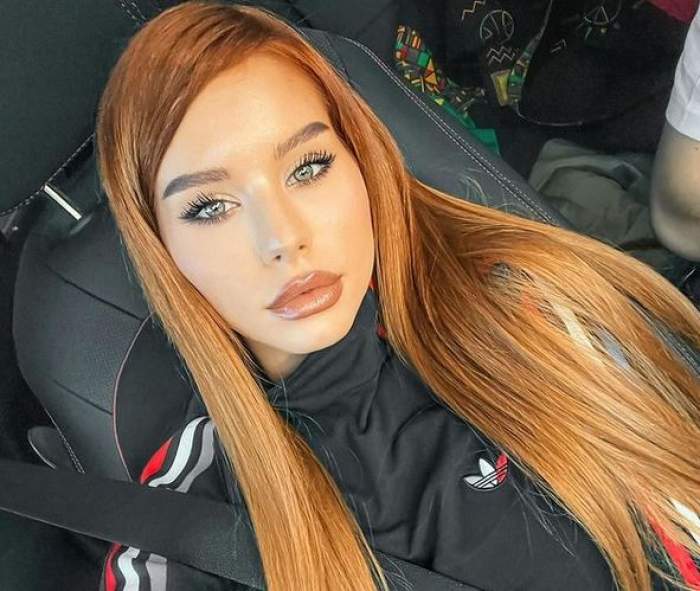 Carmen Grebenișan e în mașină. Roșcata poartă o bluză de trening neagră cu dungi albe, gri și roșii și își face un selfie.