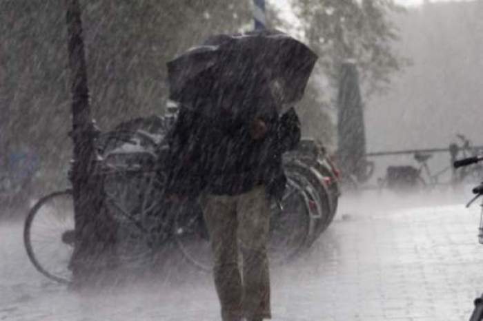 Un om care merge cu umbrela în mână, prin vânt și ploaie