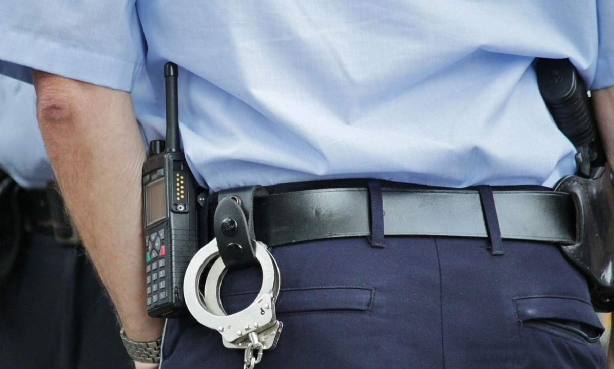 Imagine simbol cu un agent de poliție. Omul legii are cătușe în buzunarul de la spate.