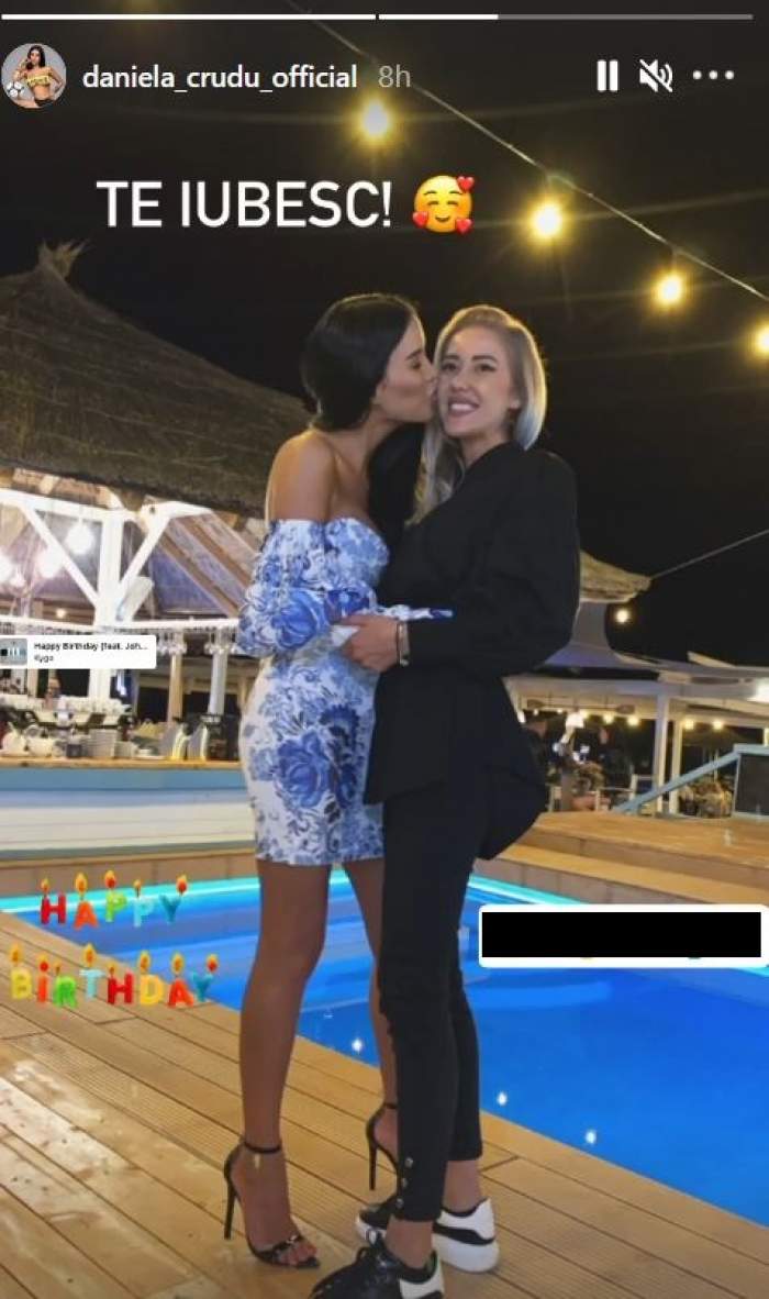 Daniela Crudu și sora ei sunt la piscină, pe marginea ei. Vedeta poartă o rochie albă cu detalii albastre și o sărută pe obraz, iar Ana Maria poartă un costum negru.