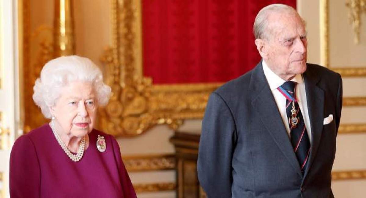 Regina Elisabeta a II-a poartă o rochie mov. Prințul Philip e îmbrăcat cu cămașă albă, iar pe deasupra are un sacou bleumarin.