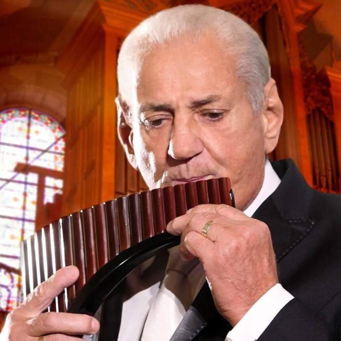 Gheorghe Zamfir poartă o cămașă albă, iar pe deasupra un costum negru. Artistul cântă la nai.