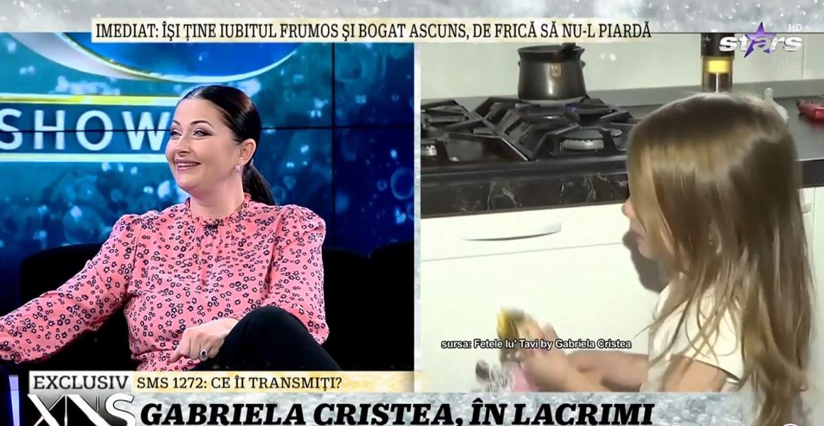 Gabriela Cristea e la Xtra Night Show. Vedeta poartă o bluză roz și pantaloni negri. Prezentatoarea zâmbește larg.
