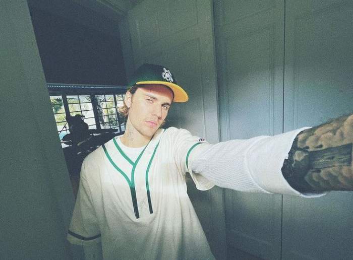 Justin Bieber poartă o șapcă verde cu cozoroc galben. Artistul își face un selfie și e îmbrăcat cu un tricou alb cu linii verzi.