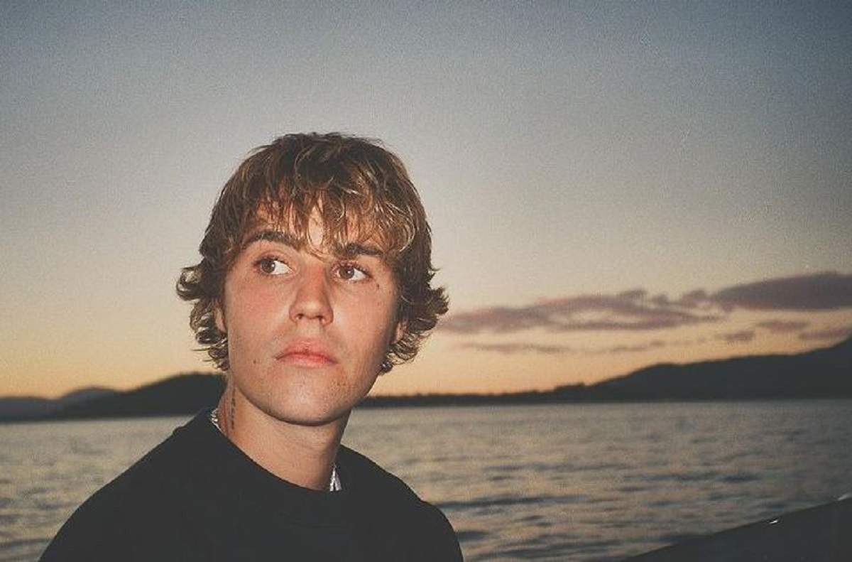Justin Bieber e pe plajă. Artistul poartă un tricou negru. În spatele lui se vede Oceanul.