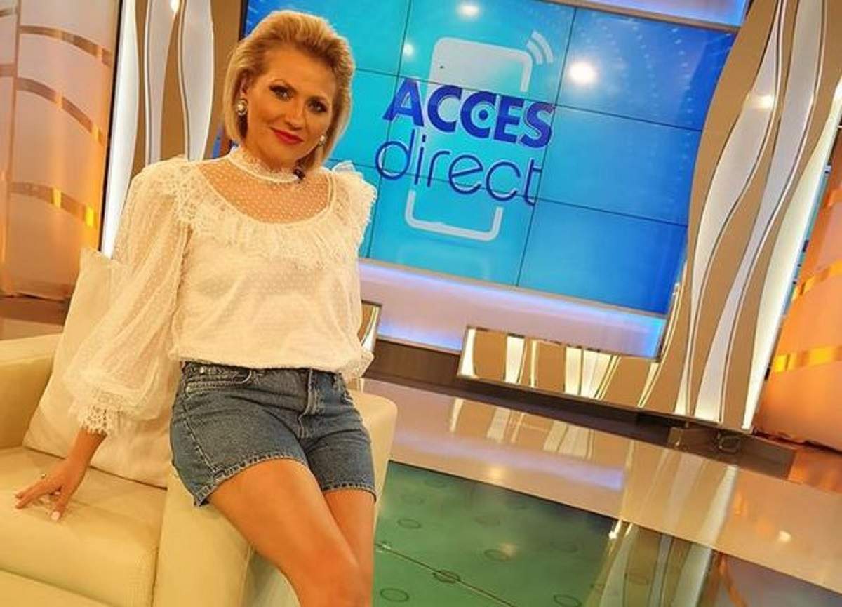 Mirela Vaida e în platoul Acces Direct. Vedeta stă pe marginea unui fotoliu alb și poartă o bluză albă și pantaloni scurți de blugi.