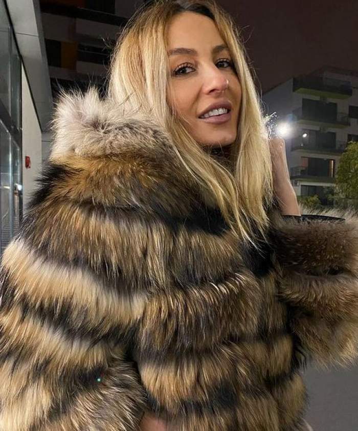 Flavia Mihășan poartă o haină de blană maronie. Vedeta zâmbește larg și se află afară.