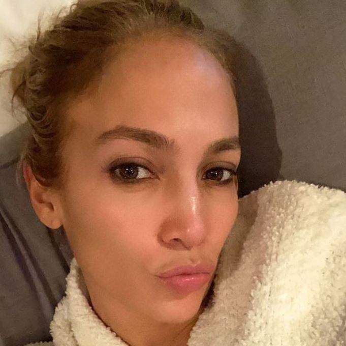 Jennifer Lopez poartă un halat de baie alb. Artista își face un selfie și ține buzele țuguiate.