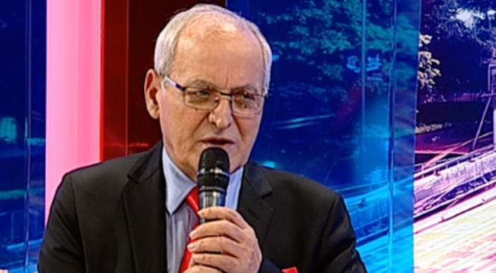 Nelu Ploieșteanu dă un interviu la Antena Stars. Artistul poartă o cămașă bleu, cravată roșie, iar pe deasupra un sacou negru.