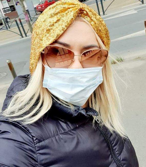 Viorica de la Clejani poartă o geacă neagră, mască de protecție, iar pe cap un turban galben din paiete. Vedeta își face un selfie pe stradă.